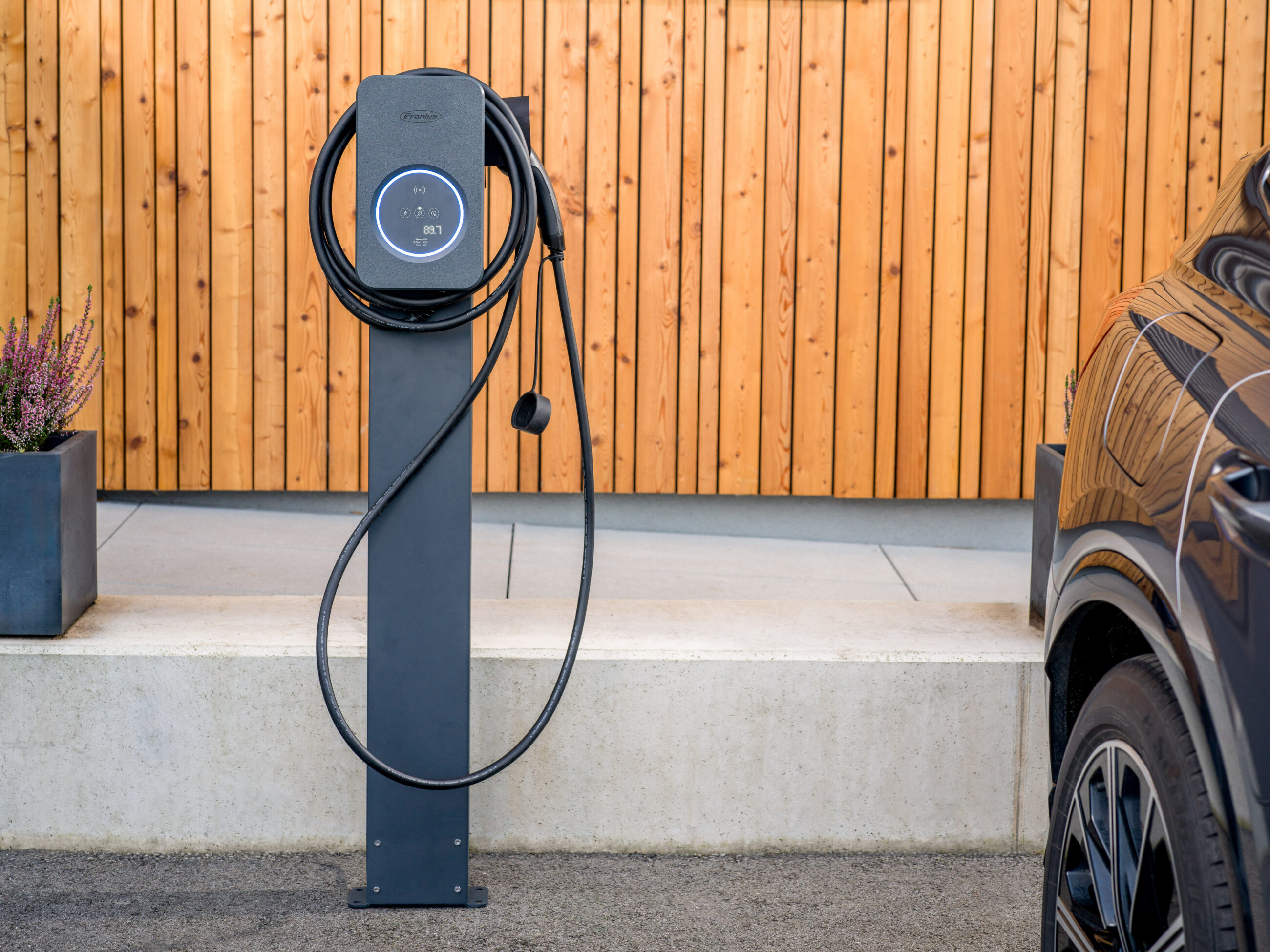 Freistehende Wallbox-Ladestation für Elektroautos auf einer Ladesäule vor einer Holzfassade; privater Ladepunkt zum Laden eines Elektrofahrzeugs am Wohnhaus.