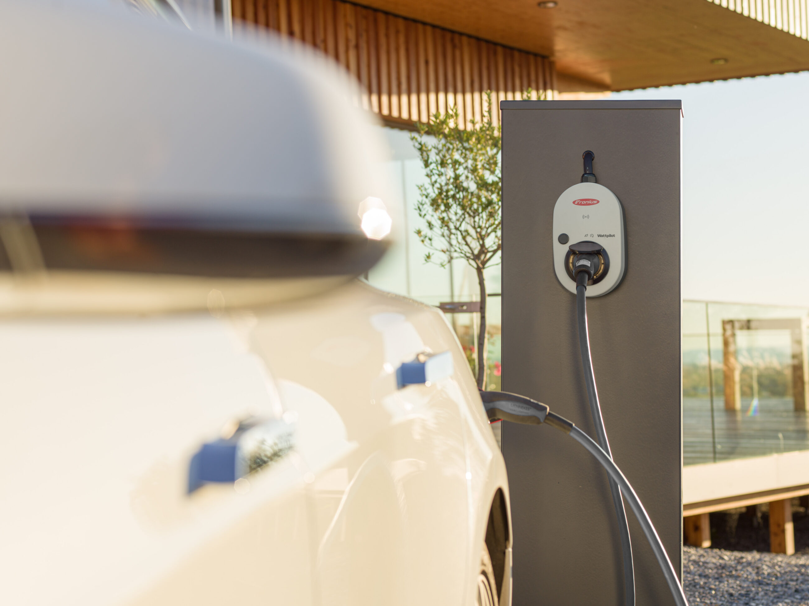 Elektroauto lädt an einer freistehenden Wallbox-Ladestation vor einem Wohnhaus; privater Ladepunkt für das Laden von Elektrofahrzeugen am Gebäude