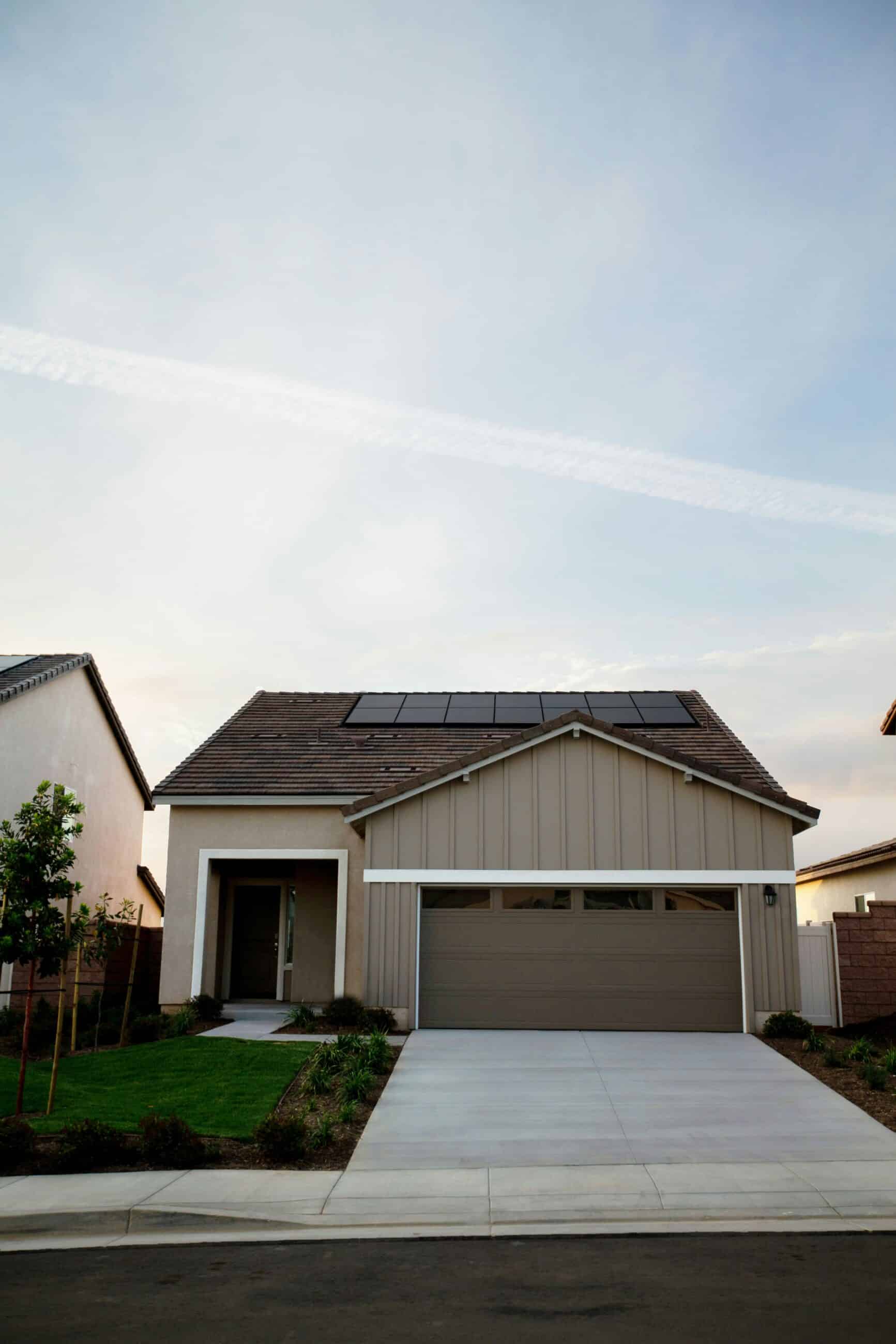 Einfamilienhaus mit Garage und auf dem Schrägdach installierten Solarmodulen, aufgenommen bei Abendlicht mit leicht bewölktem Himmel